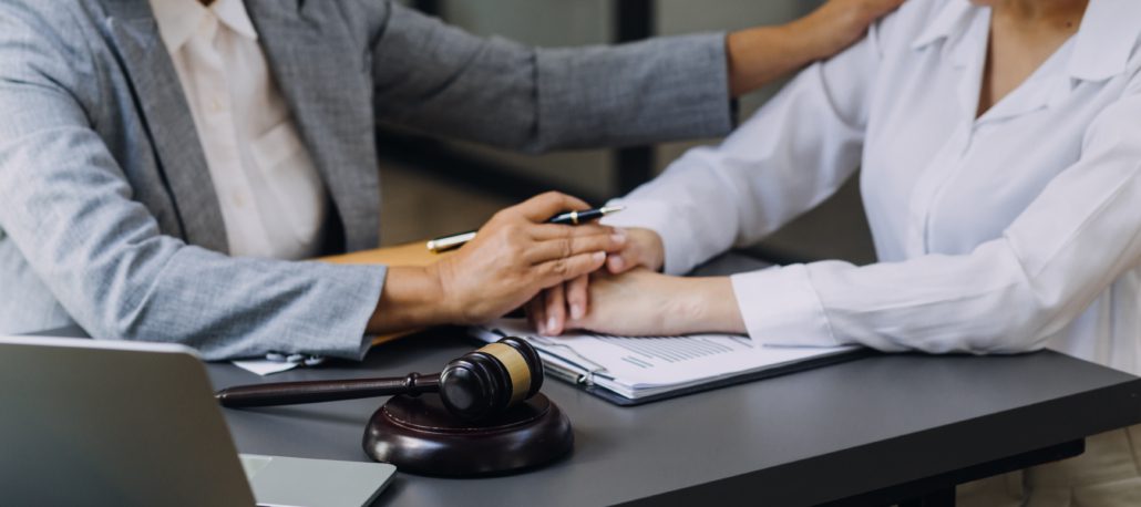 Lawyer discussing comforting and advising client with gavel on desk in office.